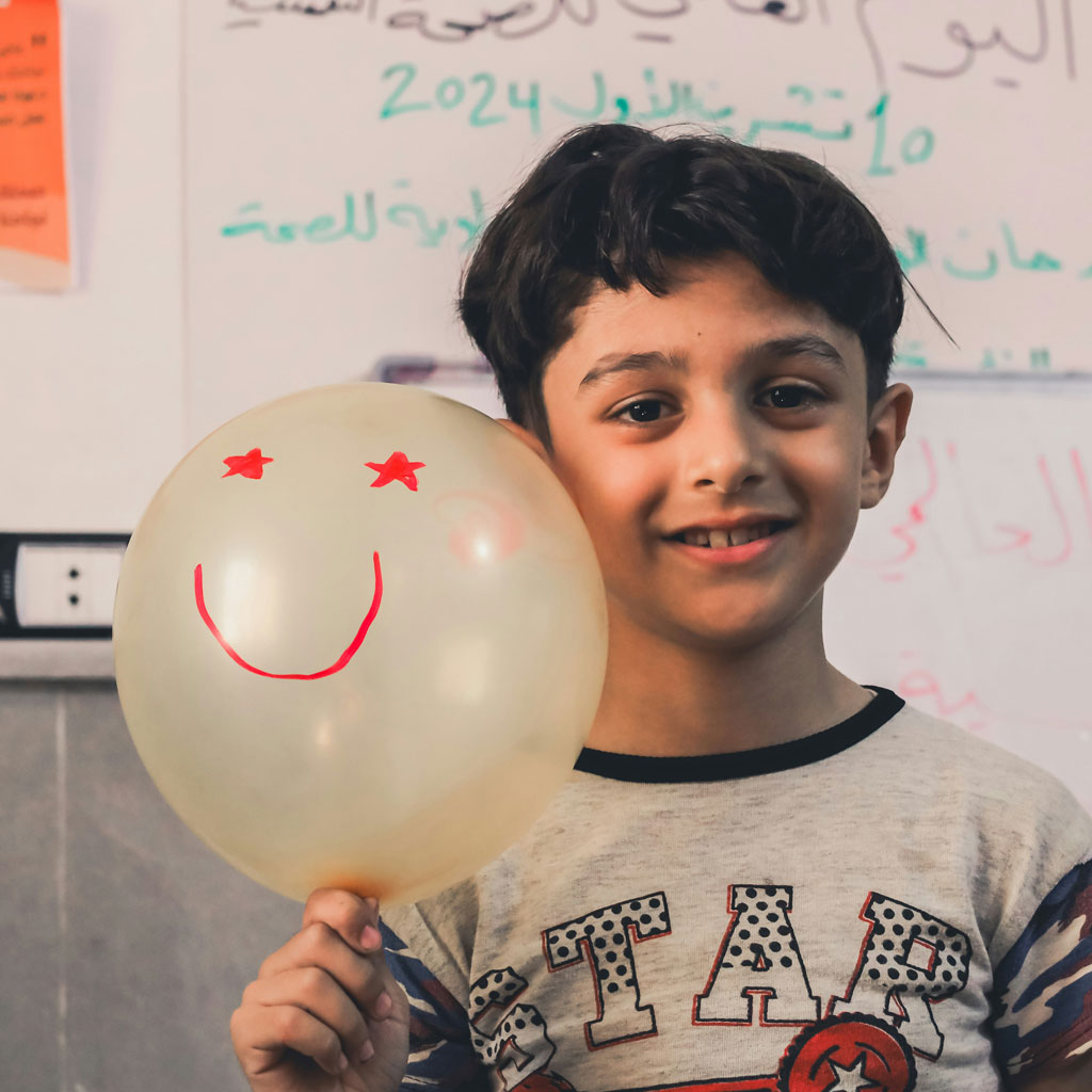 Boy holding a smiley-faced balloon, smiling.